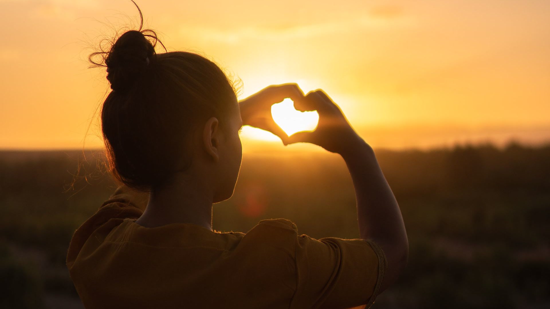 Silhouette of hands forming a heart against a warm golden sunset in Morocco